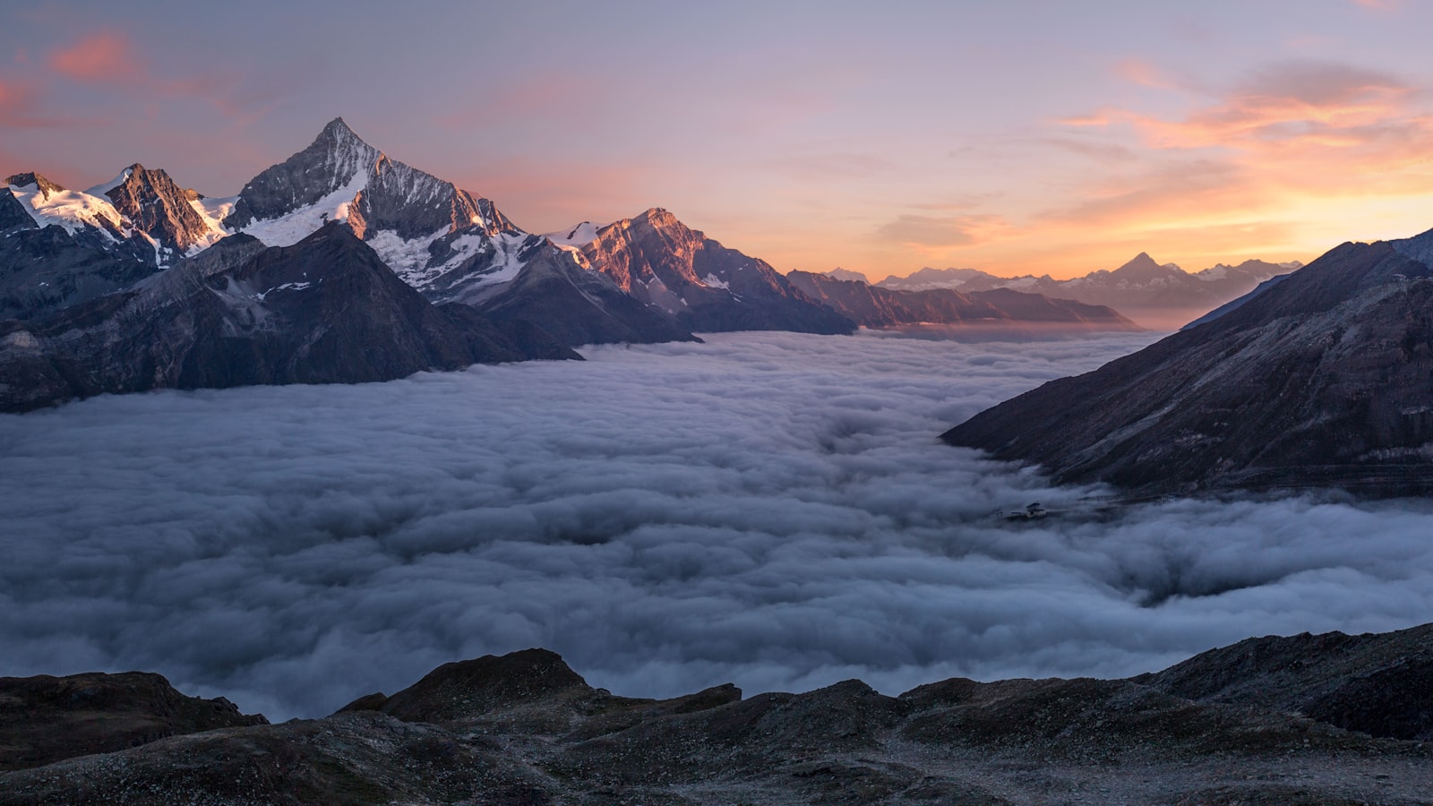 A hiker silhouetted against a glowing mountain sunrise holding a camera